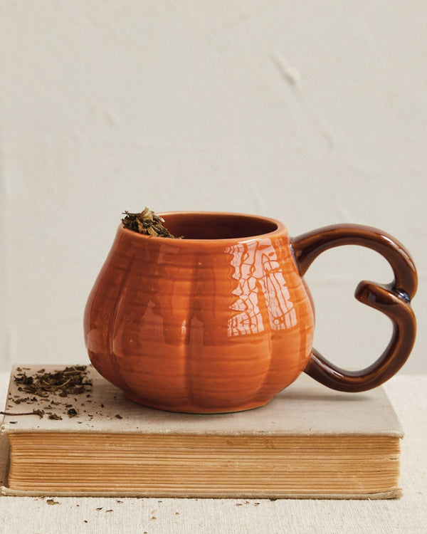 Ceramic mug with a unique handle on a book next to a small decorative item on a neutral background
