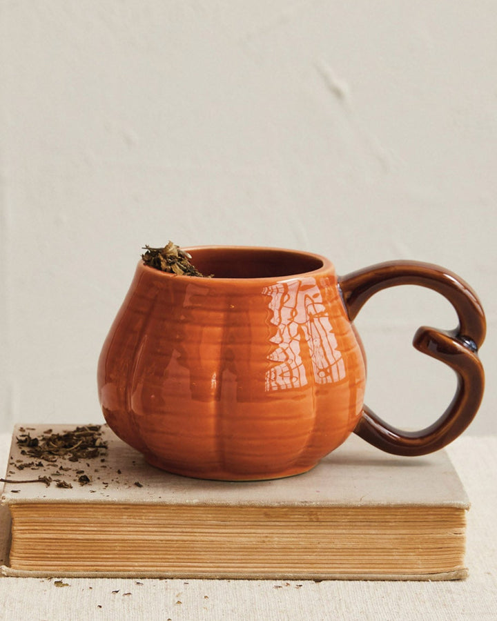Ceramic mug with a unique handle on a book next to a small decorative item on a neutral background